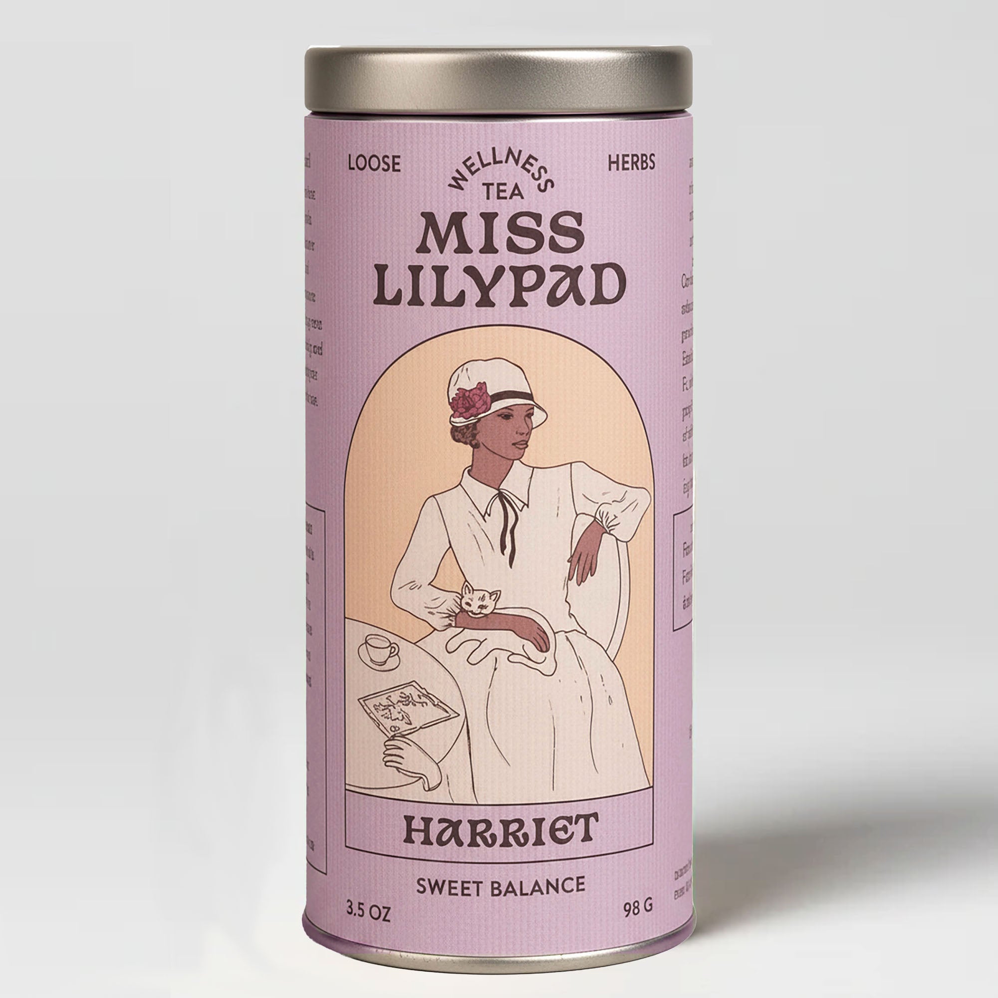 Miss Lilypad Sweet Balance Harriet loose herbal tea in a cylindrical tin canister with a lavender label and silver metal lid and base. An illustration of a woman wearing a hat and red flower sitting down holding a cat next to a table with tea cup and glovew