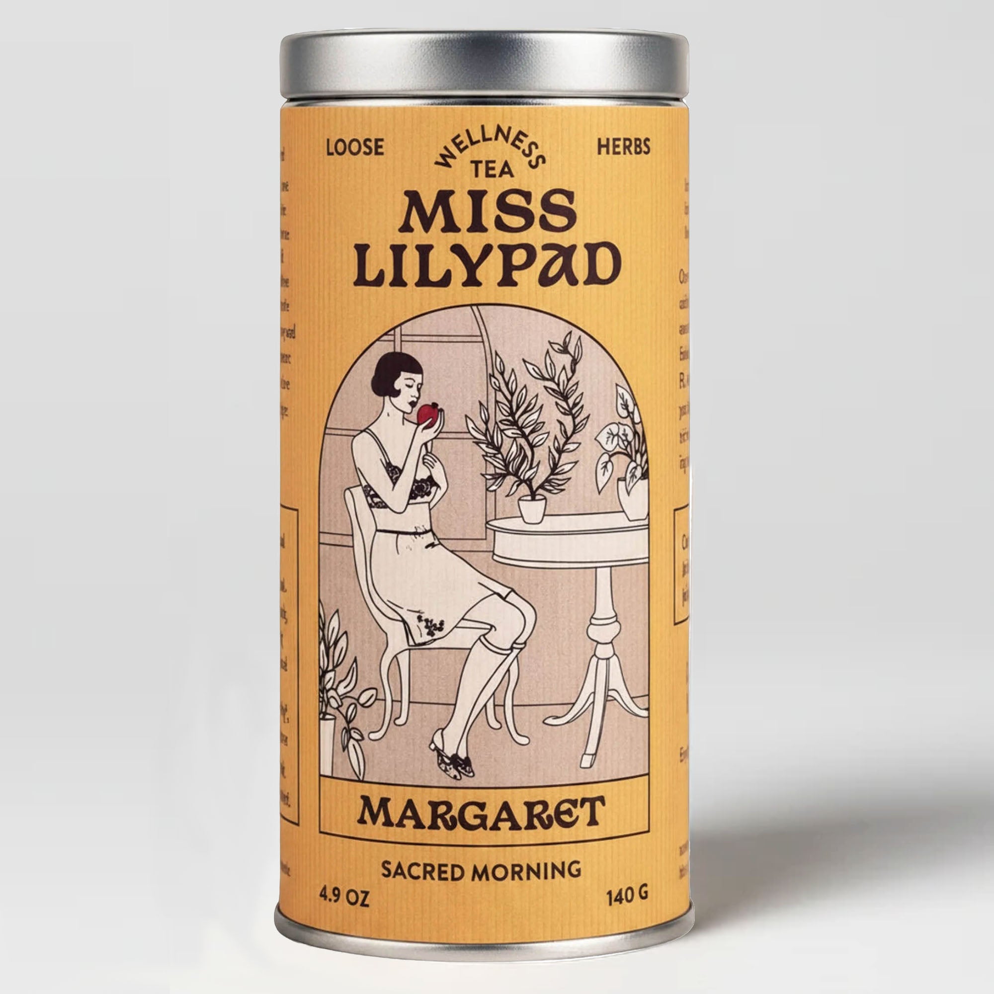 Miss Lilypad  Sacred Morning  Margaret loose herbal tea in a cylindrical tin canister with an orange label and silver metal lid and base. An illustration of a woman holding a red pomegranate sitting on a table with plants